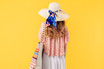 summer young woman in a summer hat, standing with her back to the camera on a yellow background