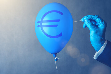 Euro currency symbol on blue balloon in coronavirus time. Man hold needle directed to air balloon. Concept of finance risk.