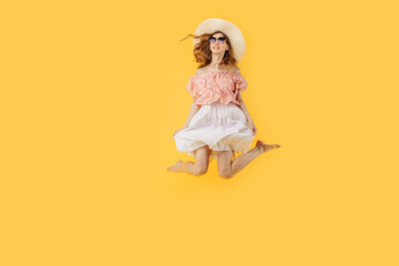 happy girl in a summer hat and sunglasses in summer, jumping high on an yellow background