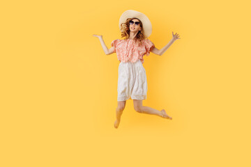 happy girl in a summer hat and sunglasses in summer, jumping high on an yellow background