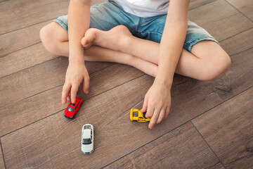 Kid barefoot sits on wooden floor in lotus position and plays mini toy color cars. Playful playing...