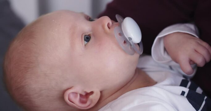Closeup shot of a newborn baby girl sucking on a pacifier in the arms of her mother.