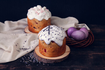 Easter cakes on a dark wooden background, decorated with lavender and marshmallows, and painted Easter eggs in a wicker nest.