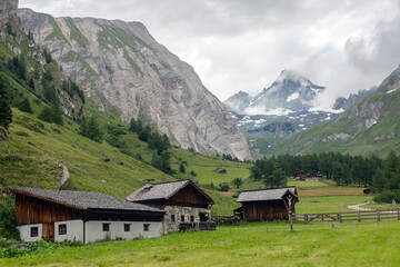 Fototapeta na wymiar Green valley with Tyrolean houses on a background of alpine peaks in the fog. Hiking travel outdoor concept, journey in the mountains, Kals am Grossglockner, Austria