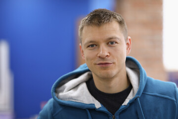 Portrait of smiling cheerful young man posing on camera in room. Happy adult wearing blue hoodie. Copy space in left side. Modeling and happiness concept