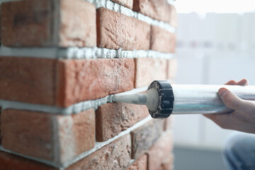 Close-up of professional worker holding fixing foam on construction site. Red brick wall in apartment. White filling foam line. New interior design. Renovation concept