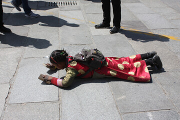 Little girl wearing traditional red cloathes with protection on hands praying in prostration in front of Jokhang temple in Lhasa on Barkhor square, Tibet