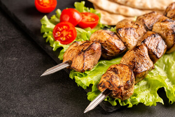 Two portions of shish kebab on a stone plate with salad.