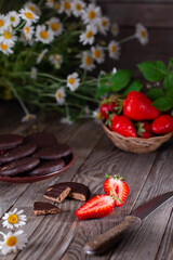 Fresh strawberries on a wooden table with a knife, chocolate chip cookies and summer camomile flowers