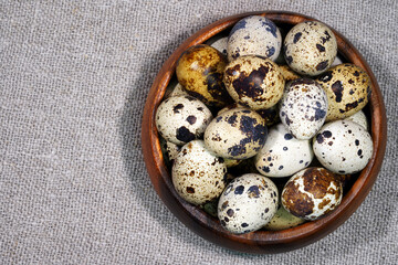 Fototapeta premium Quail eggs in a round wooden bowl on canvas, close-up, macro. Eggshell stains. Spotted pattern on the eggs. Dietary healthy foods. Egg. 