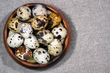 Fototapeta premium Quail eggs in a round wooden bowl on canvas, close-up, macro. Eggshell stains. Spotted pattern on the eggs. Dietary healthy foods. Egg. 