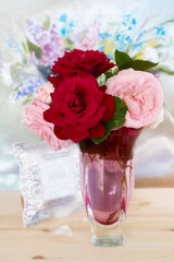 Bouquet of lively red and pink roses in a glass vase on the table, floral background. Flowers of hybrid tea roses with scarlet and pink delicate petals.