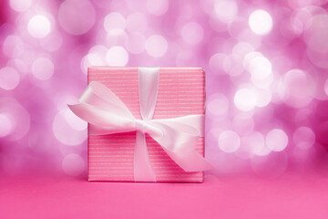 Gift box with white bow over defocused lights. Pink color composition