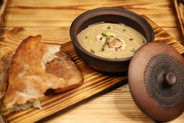 Thick mushroom cream soup in a clay pot. Proper balanced nutrition. Vegetarian vegetable soup. Dish menu on a wooden board. Fragrant hot food. High-calorie food. Organic products. Restaurant menu.