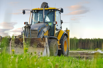 Fototapeta premium Yellow Excavator. yellow tractor on the field. Construction Machinery On Field. large yellow wheel loader aligns a piece of land for a new building. Tractor On Farmland.