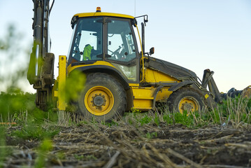 Obraz premium Yellow Excavator. yellow tractor on the field. Construction Machinery On Field. large yellow wheel loader aligns a piece of land for a new building. Tractor On Farmland.