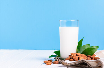 lactose-free milk concept, glass with almond milk nuts on a white table on a blue background