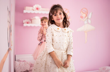 Adorable girls, sisters, twins standing on the bed in their lovely pink room