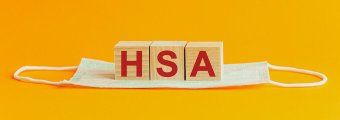 HSA word is written on wooden cubes lying on a medical mask. Concept. Health Savings Account.