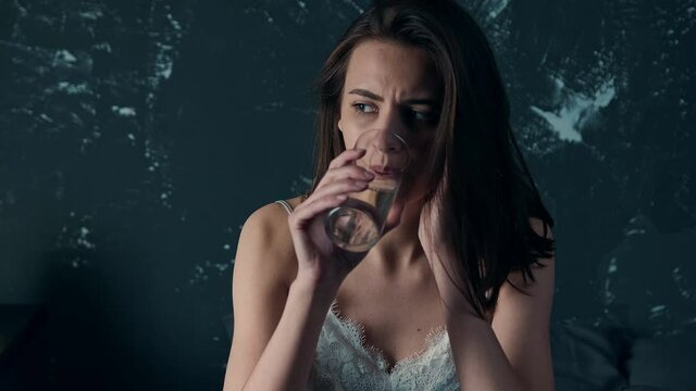 Close up of Young Attractive Woman in White Nightgown Staying in Bed Feeling Unwell or Suffering from a Bad Headache, Drinking Water. Woman with Insomnia. Sleeping Disorder.