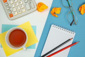 Notebook for notes, note sheets, calculator and pencils, glasses and cup with tea. White and blue background.