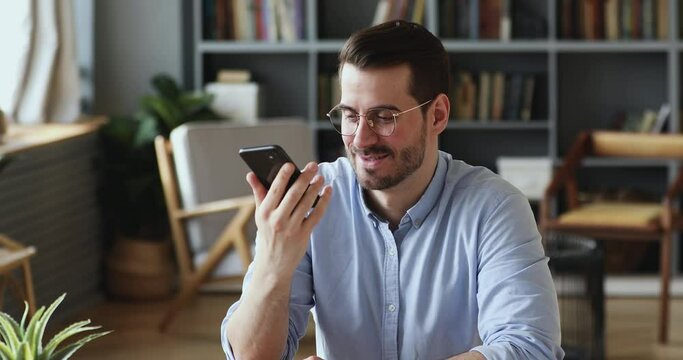 Happy handsome businessman dictating audio message on smartphone in social network application. Smiling young man activating voice assistant, having mobile conversation or search information online.