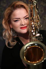 Portrait of a charming blonde with a saxophone in her hands. Beautiful girl in a black evening...