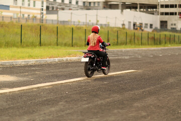 A girl motorcyclist in a red jacket passes an exam in a driving school. A woman rides a bike. Woman in a red helmet rides a motorcycle.