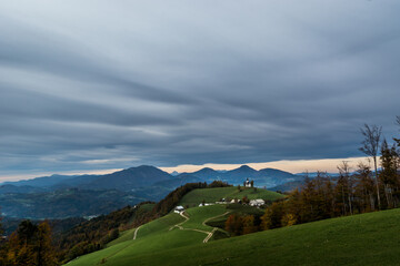 Amazing landscape view in Slovenia mountains. Small church on hilltop. Slopes covered with green grass. Cloudy sky over Alps mountains. Idyllic countryside village