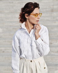 Stylish woman with yellow sunglasses posing outdoors.