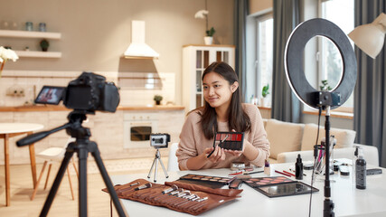 This is the future. Asian female blogger showing cosmetic products while recording a tutorial video for her beauty blog using camera at home
