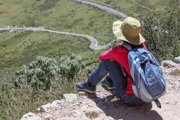 Hiking trail around Drepung monastery near Lhasa with a tourist woman wearing a hat sitting and looking at distance, Tibet, Asia