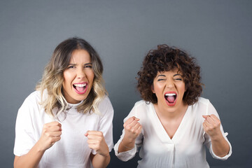 Portrait of beautiful brunette female looks with excitement at camera, keeps hands raised over head, notices something unexpected, isolated over white wall. Lovely women reacts on sudden news.