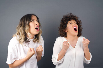 Brunette girl friends excited and glad to achieve victory, clench fists, scream in excitement with closed eyes, happy to pass all exams at university, successful people.