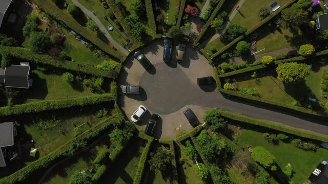Aerial top view of vehicles on driveway amidst houses in town, drone ascending over suburb on sunny day - Copenhagen, Denmark