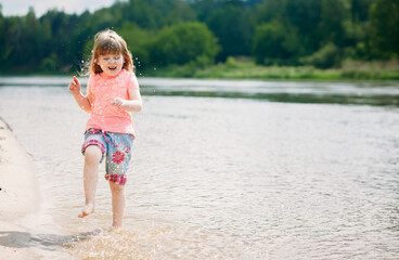 Beautiful positive child running on the water, little girl with long developing hair have fun