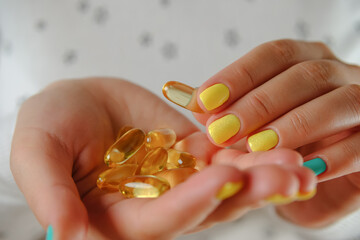 Woman hand holds yellow medication capsules of omega 3. Girl accepts the fish oil.