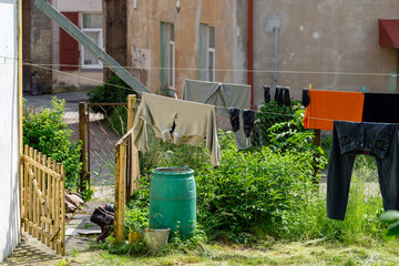 Naklejka premium Clean different laundry are dried outside in the yard on a clothing line in the city. Black shoes are ventilated at the gates. On blurred old houses background. Concept of cleanliness and cleansing