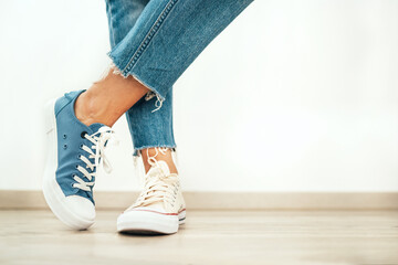 Teenager's feet posing in casual different colors beige and blue new sneakers on the white wooden floor close up image. Vintage style in modern fashion world concept image.