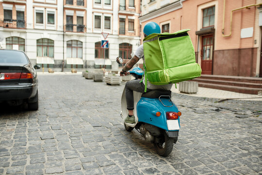 You Select, We Deliver. Delivery Man In Helmet With Thermo Bag Or Backpack Riding A Motor Scooter Along The City, Delivering Food. Courier, Delivery Service Concept