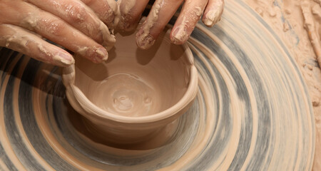 Woman in process of making clay bowl on pottery wheel