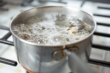 A view of a saucepan with boiling water on the stove top, in a kitchen setting.
