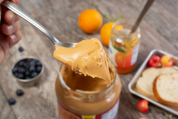 A view of a spoon scooping out a heap of peanut butter from the jar, in a still life setting.