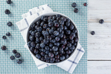 A top down view of a bowl of fresh blueberries, on a wooden table surface.