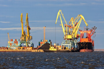 Fototapeta na wymiar Seaport in the Arctic. A cargo ship near the pier of the sea port. Large port cranes. Logistics, shipping and freight in the Arctic. Stevedore services. Anadyr seaport, Chukotka, Far East Russia.