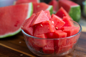 A view of a glass bowl full of chopped watermelon, in a kitchen or restaurant setting.