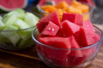 A view of several glass bowls of chopped melon chunks, featuring a bowl of seedless watermelon.