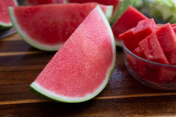 A view of a large slice of watermelon next to a glass bowl filled with chopped melon chunks.