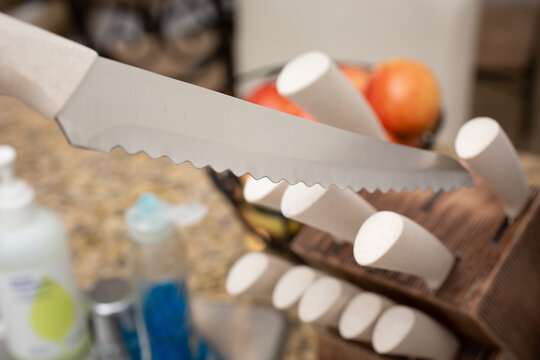 A view of a serrated knife being pulled out of a knife block, in a kitchen setting.