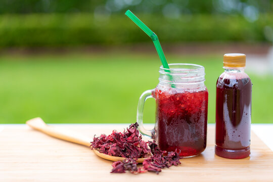 Cold beverage glass of roselle juice with colorful straw in wooden table Thai herb juice and refreshment cold drink..
